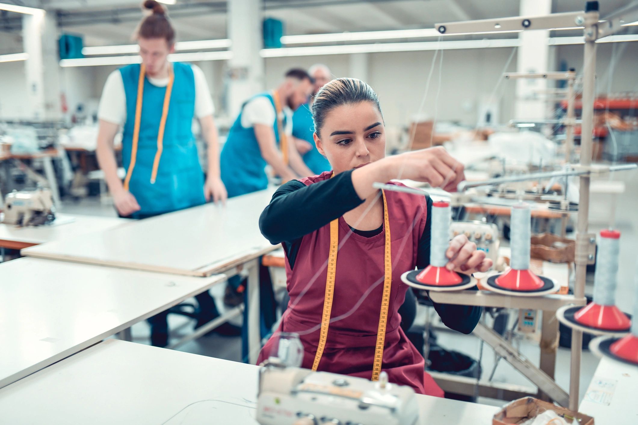 Textile worker setting up threads while colleagues measure cloth